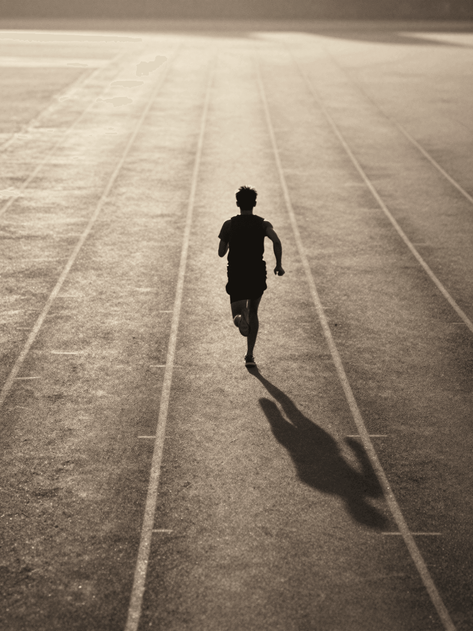 A lone runner in motion seen from behind on an empty track at dawn, one long shadow in warm light - performance measured in silence.